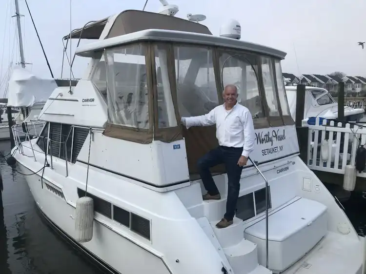 Man posing on the back of a docked white yacht.