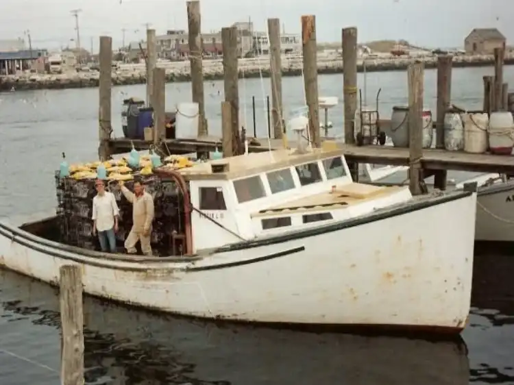 A white fishing boat docked at a harbor with people on board.