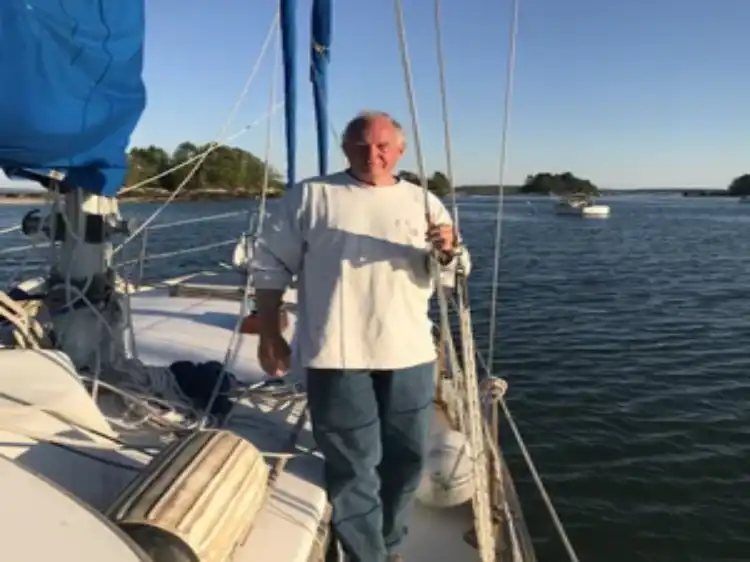 Man standing on a sailboat deck holding a fishing rod.