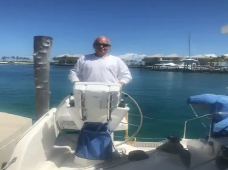 Man steering a boat in a marina on a sunny day.