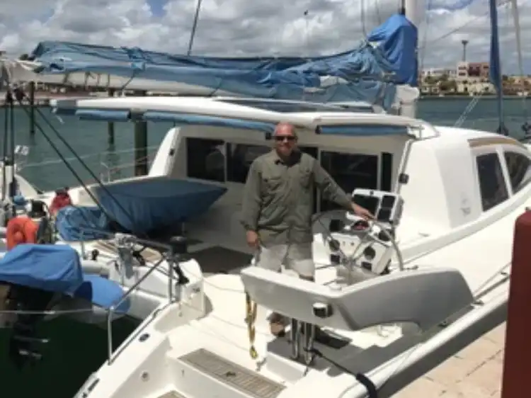 Man standing on a white sailboat docked at a marina on a cloudy day.