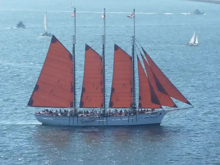 A traditional sailing ship with red sails on calm blue waters.