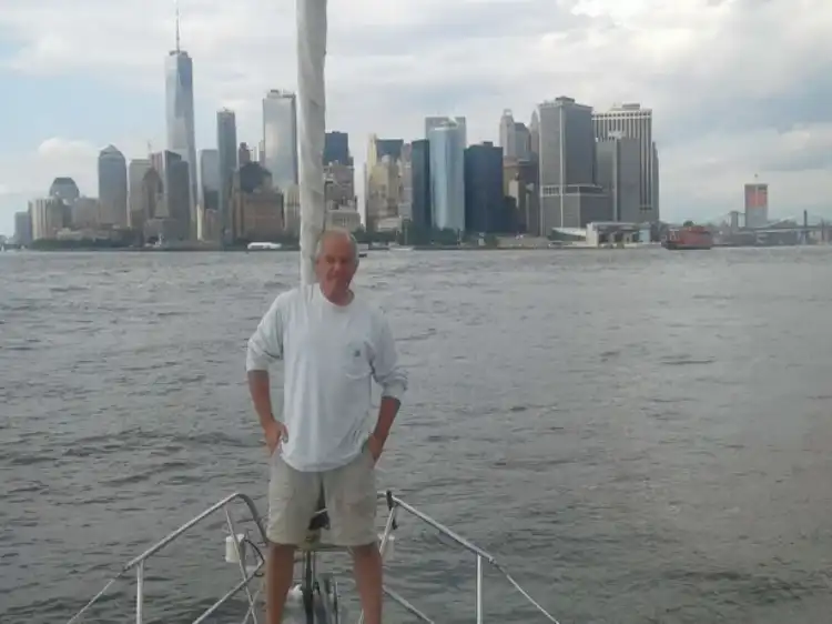 Man standing on a boat with a city skyline in the background.