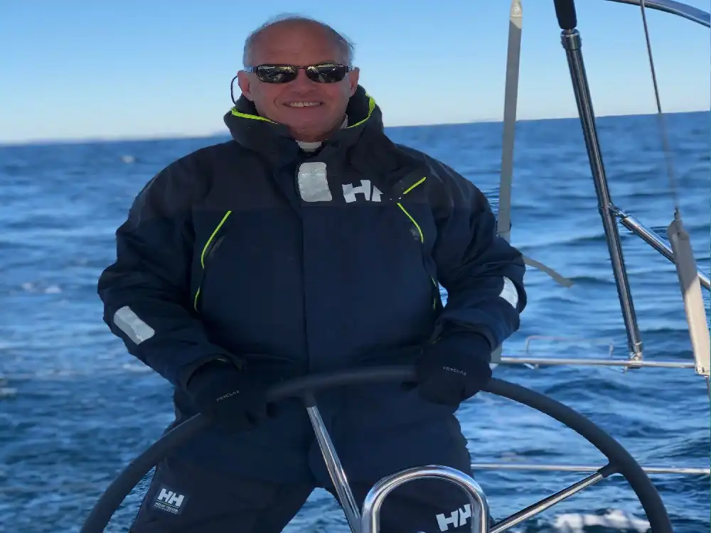 Man in sailing gear steering a boat on a sunny day.