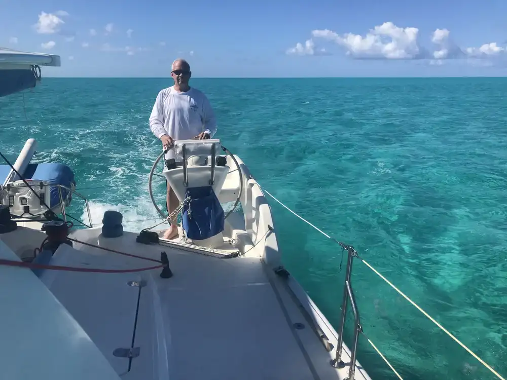 Person steering a boat on clear turquoise waters under a blue sky.