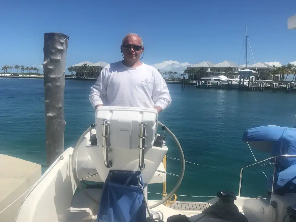 Man steering a boat in a sunny marina.