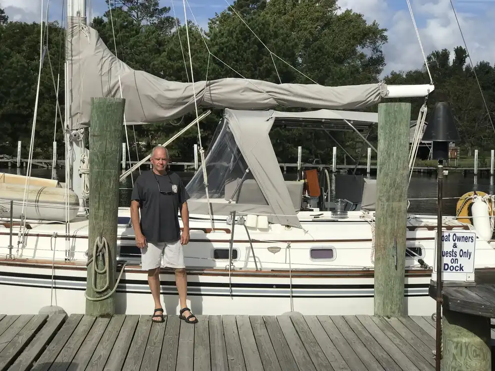 Man standing on a dock beside a sailboat with furled sails.