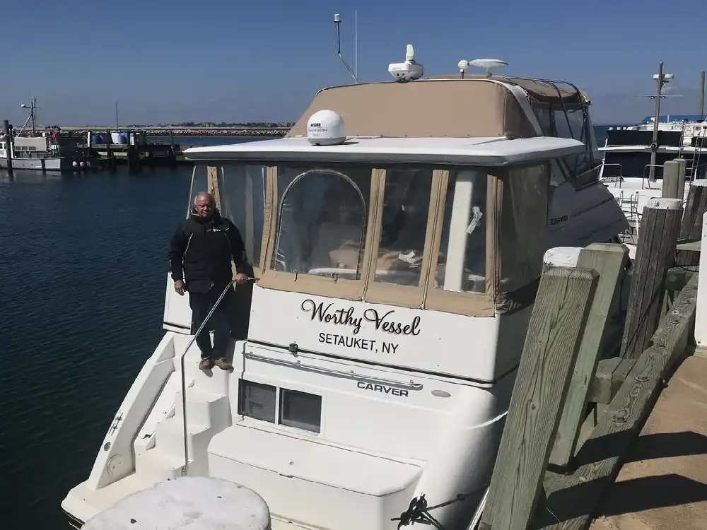 Man standing on a white yacht docked at a marina.