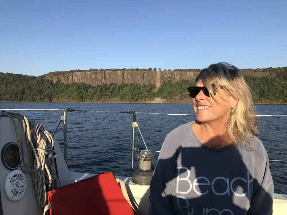Woman enjoying a sunny day on a boat with cliffs in the background.