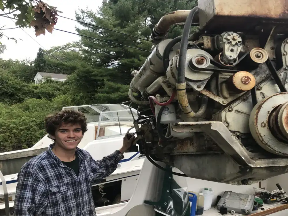 Young man posing with a large engine on a boat.