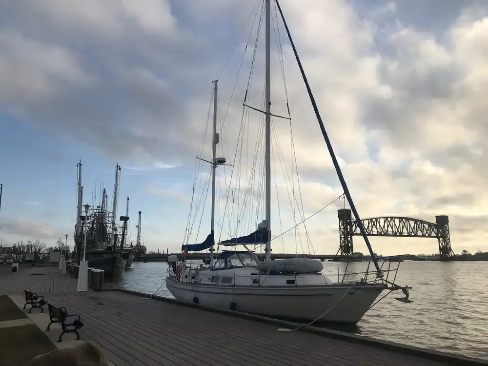 Sailboat docked at harbor under a cloudy sky near a bridge.