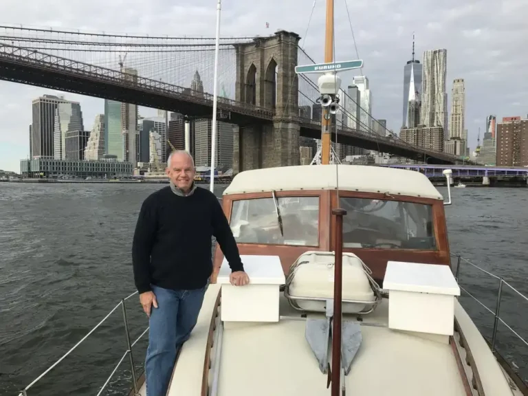 Man standing on a boat near Brooklyn Bridge in New York City.