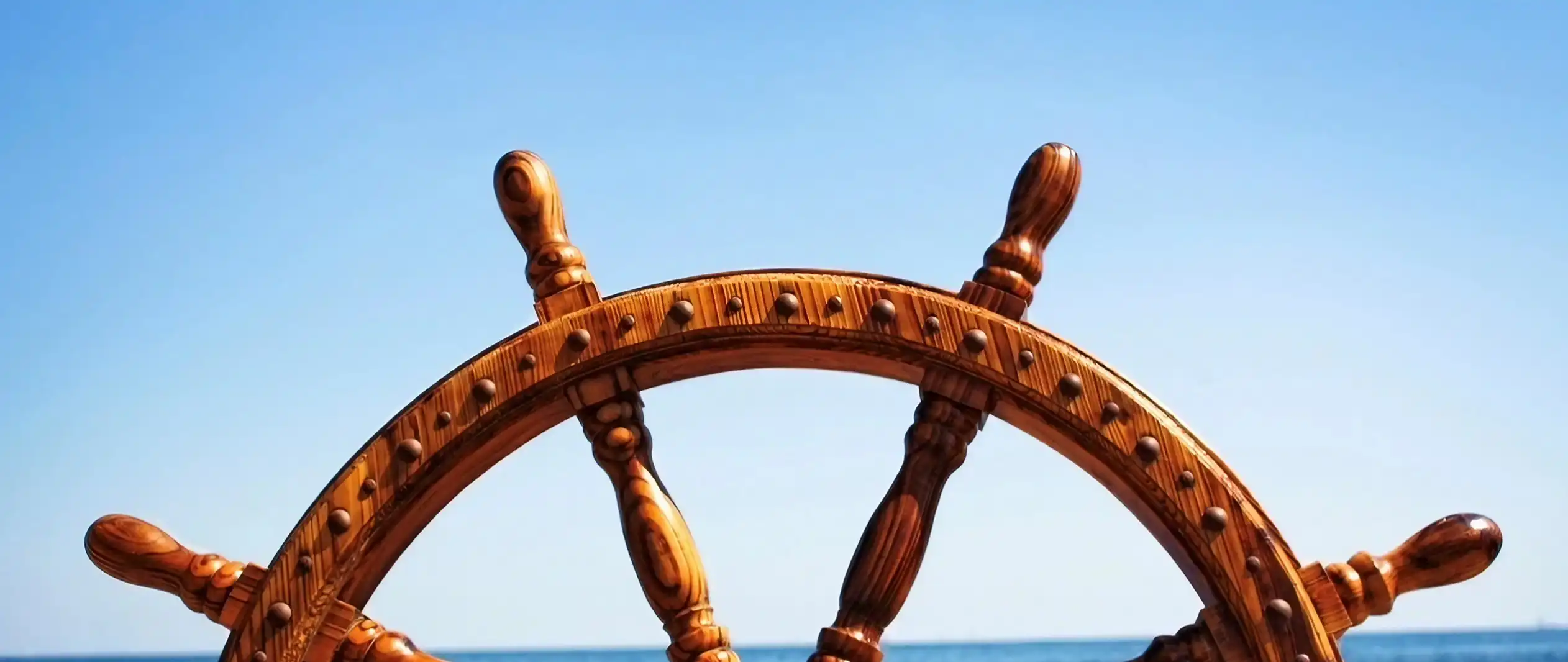 Close-up of a wooden ship's steering wheel against a clear blue sky.