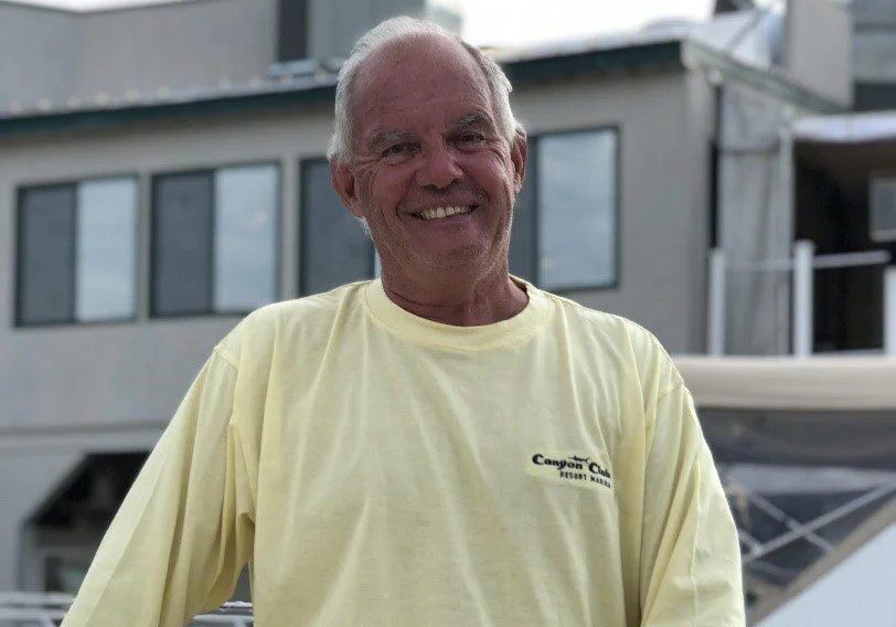Smiling man in a yellow shirt outdoors near buildings.