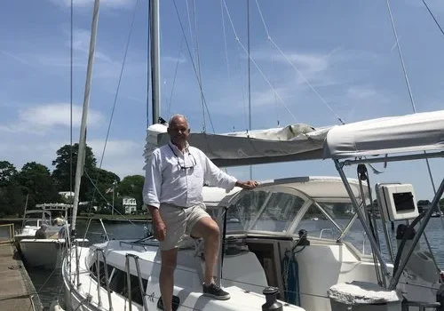 Man standing on a sailboat docked in a marina on a sunny day.
