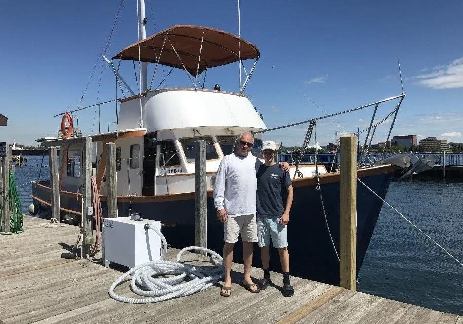 Two men posing on a dock beside a boat under a clear sky.