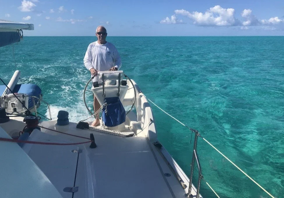 Person steering a boat on clear turquoise waters under a sunny sky.