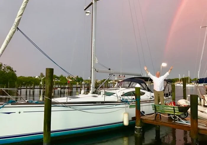 Man joyfully jumping on dock near sailboat at marina.