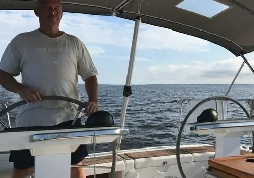 A man steering a sailboat on calm waters under a clear sky.