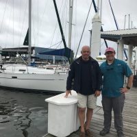 Two men standing on a dock with sailboats in the background.