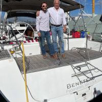 Two men standing on the back deck of a sailboat named Beneteau.