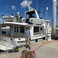 A man standing on a dock next to a yacht under a clear blue sky.