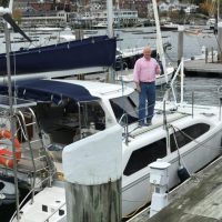 A man in a pink shirt standing on a docked white sailboat.