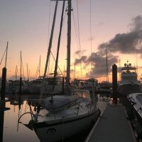 Sailboats docked at sunset in a calm marina.