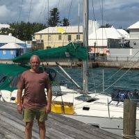 Man standing on dock near sailboats under cloudy sky.