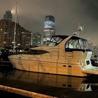 A yacht docked at night with city buildings in the background under a cloudy sky.