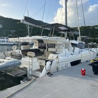 A sleek white catamaran docked at a marina with hills in the background.
